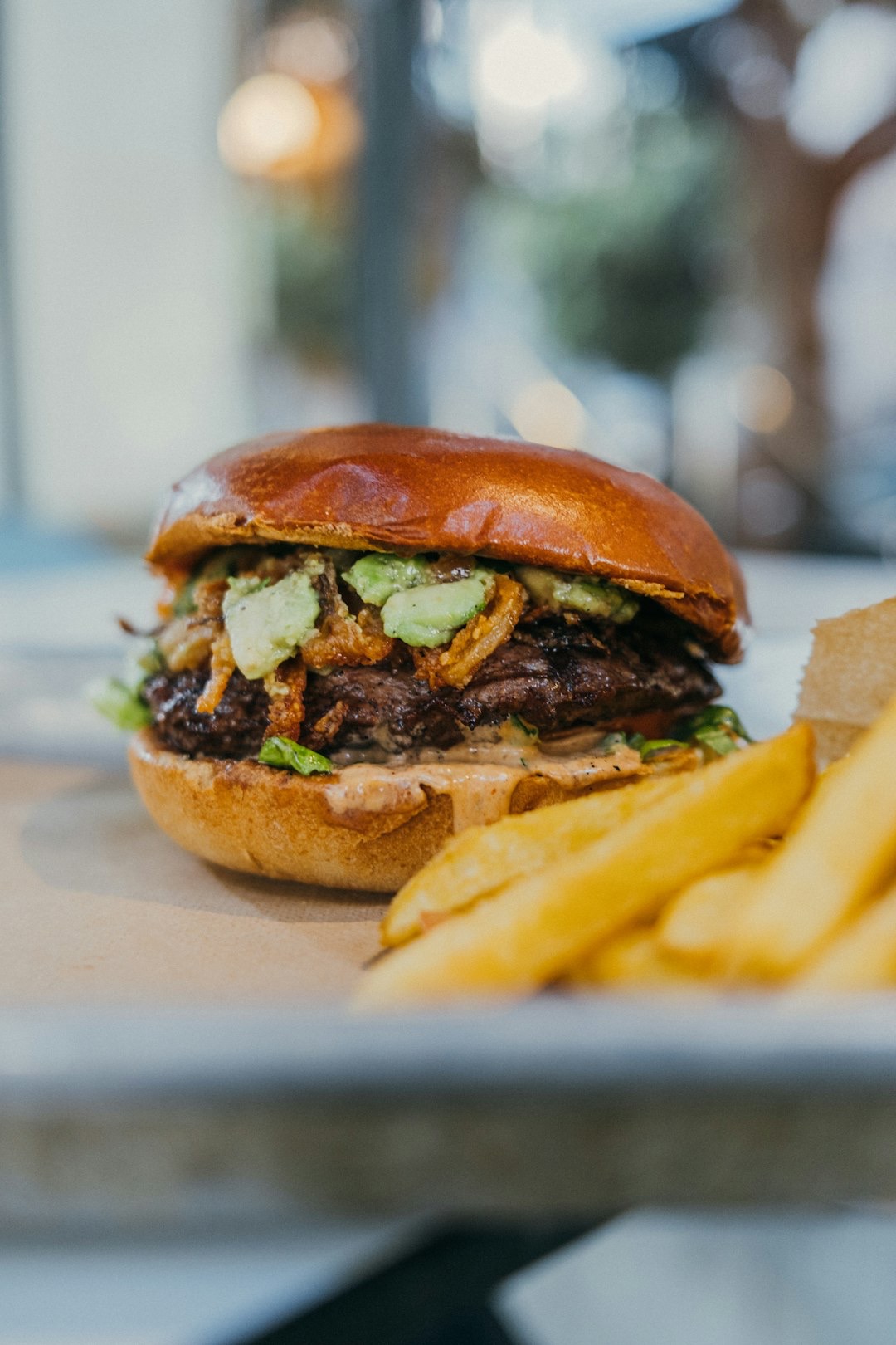 Gourmet beef burger with avocado and fries on brown paper.